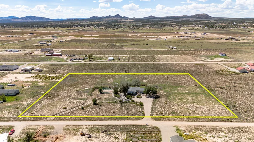 Expansive property with a single-story residence and detached garage, featuring a paved driveway and surrounding natural landscaping