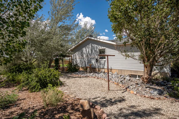 Gravel pathway with rock edging, mature trees, dense shrubs, and a partial view of the residence with horizontal siding