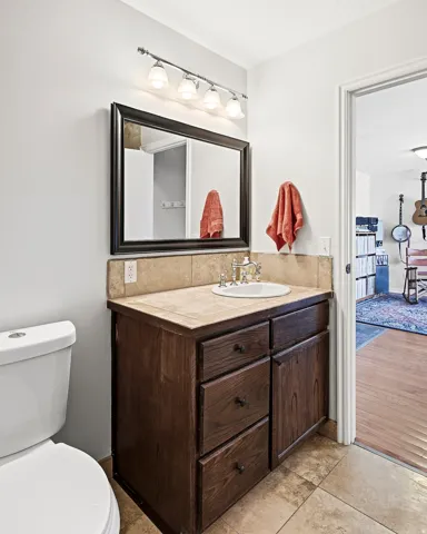 Vanity with a tiled countertop, ceramic sink, and wood-finish cabinetry featuring black hardware