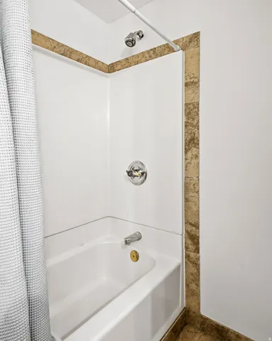 Bathtub with a shower head, chrome fixtures, and decorative tile accents