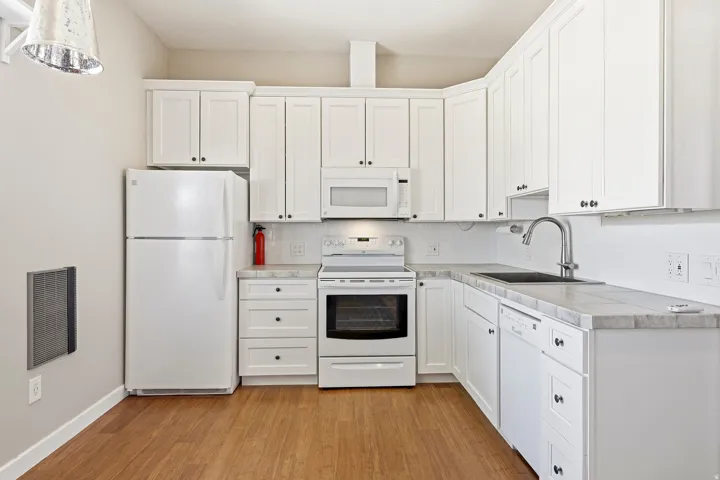 Wood-finish flooring with white cabinetry, tile countertops, stainless steel sink, and white appliances