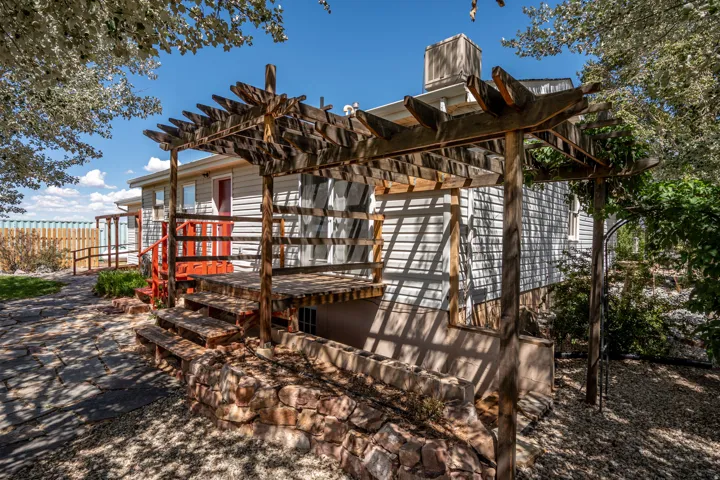 Wooden pergola with a stone retaining wall, exterior wood siding, red painted railing, and flagstone pathway