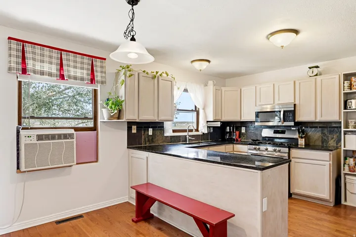 Kitchen featuring wood-finish flooring, light-toned cabinetry, dark countertops, stainless steel appliances, and a built-in kitchen island