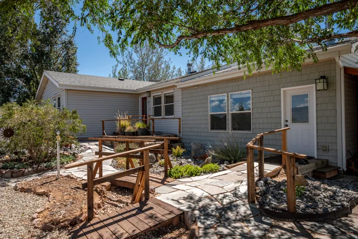 Exterior featuring light gray siding, wood-look shake siding, a stone pathway, a wooden ramp, and mature landscaping