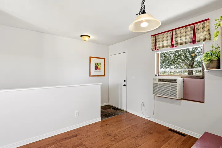 Wood-finish flooring throughout, featuring a window-mounted air conditioning unit, and a built-in shelf
