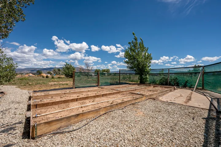 Expansive outdoor area featuring multiple raised garden beds, a gravel ground covering, and a perimeter fence with green screening
