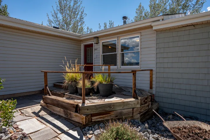 Wood-finish deck with railing, light-colored siding, and a red entry door