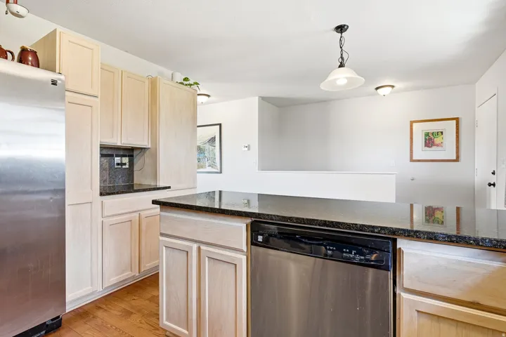 Kitchen featuring light wood-finish cabinetry, dark stone countertops, stainless steel appliances, and wood-finish flooring