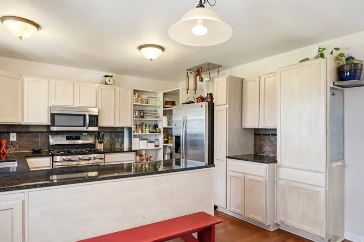Kitchen featuring stainless steel appliances, dark stone countertops, light-toned cabinetry, a tiled backsplash, and recessed overhead lighting