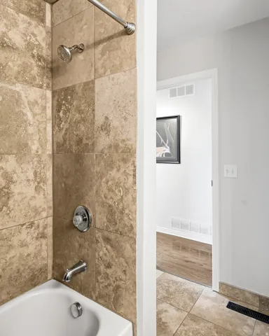 Bathtub featuring chrome fixtures and natural stone-finish wall tile