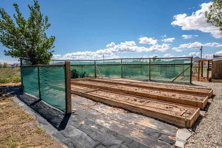 Outdoor garden area featuring multiple wooden raised garden beds, surrounded by a green shade cloth fence