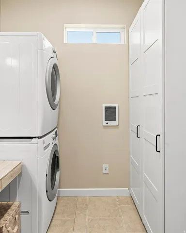 Built-in storage cabinetry with matte black hardware, stacked laundry appliances, and a wood-finish countertop