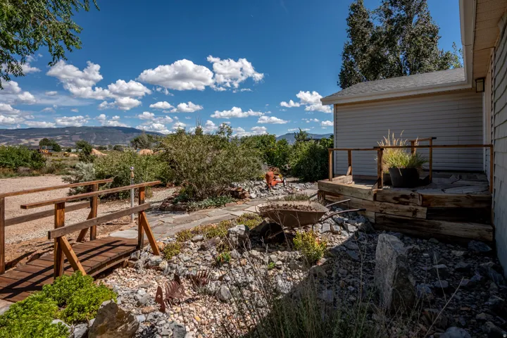 Wood bridge structure, stone-paved pathway, wood deck with railings, vinyl siding, and mountain backdrop