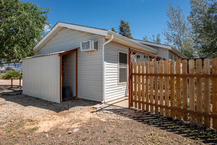 Siding exterior with a covered storage area, a window unit air conditioner, and a wood picket fence