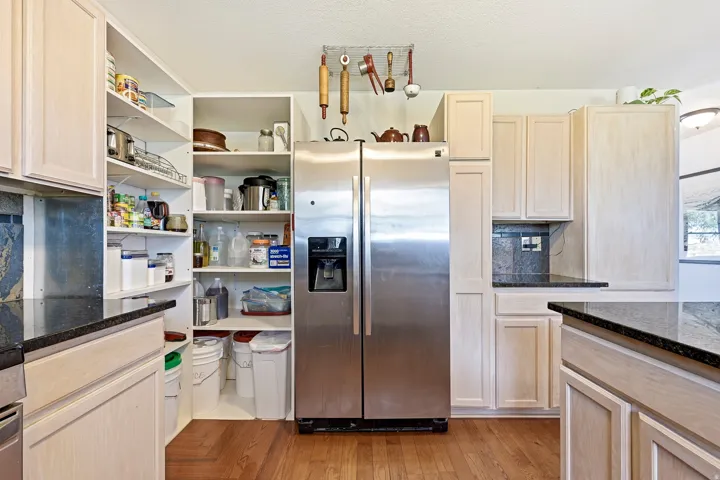 Stainless steel side-by-side refrigerator, ample cabinetry with light-toned wood-finish doors, dark countertops, and extensive built-in pantry shelving