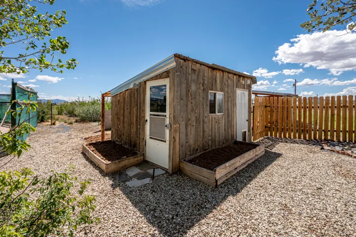 Wood-sided outbuilding with a white entry door, window, and two raised garden beds