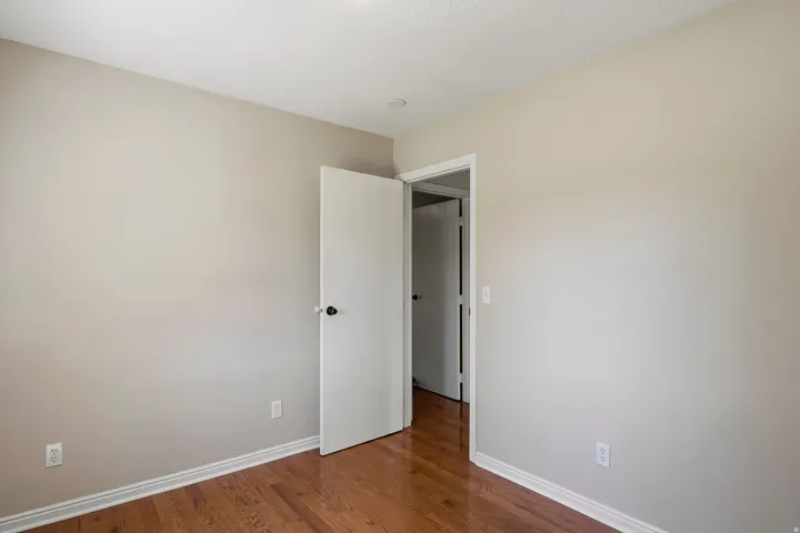 Bright corner bedroom with warm wood-finish flooring, neutral painted walls, and abundant natural light