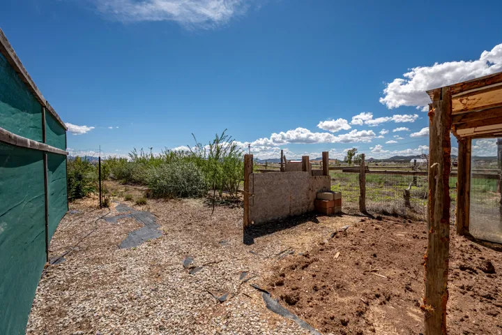 Gravel surface, open-air structure, partial privacy screening, natural vegetation, and rustic fencing