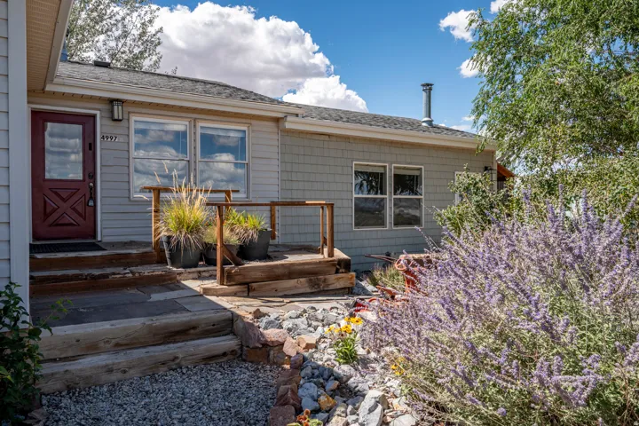 Charming single-story home with a thoughtfully landscaped exterior featuring native plantings, decorative rock hardscaping, and wooden deck with stepped entry