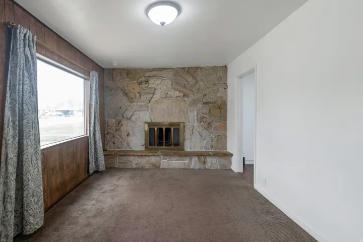 Stone-clad fireplace with a brass firebox, flanked by a picture window and wood-paneled walls