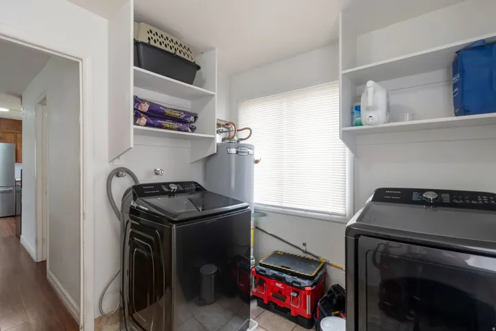 Dedicated laundry area featuring white shelving, a window with blinds, and tiled flooring