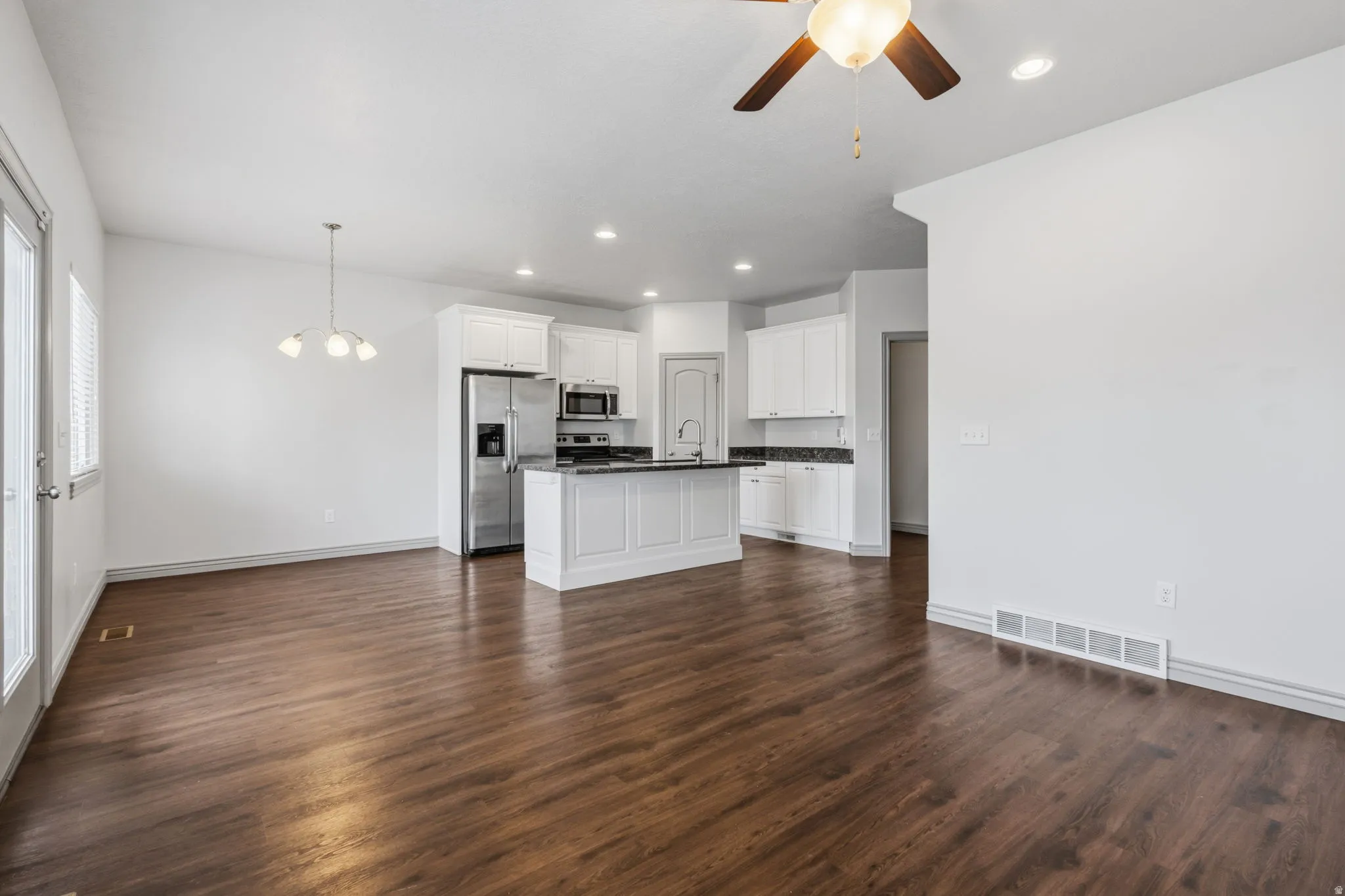 Wood-finish flooring, white cabinetry, stainless steel appliances, recessed lighting, and a ceiling fan