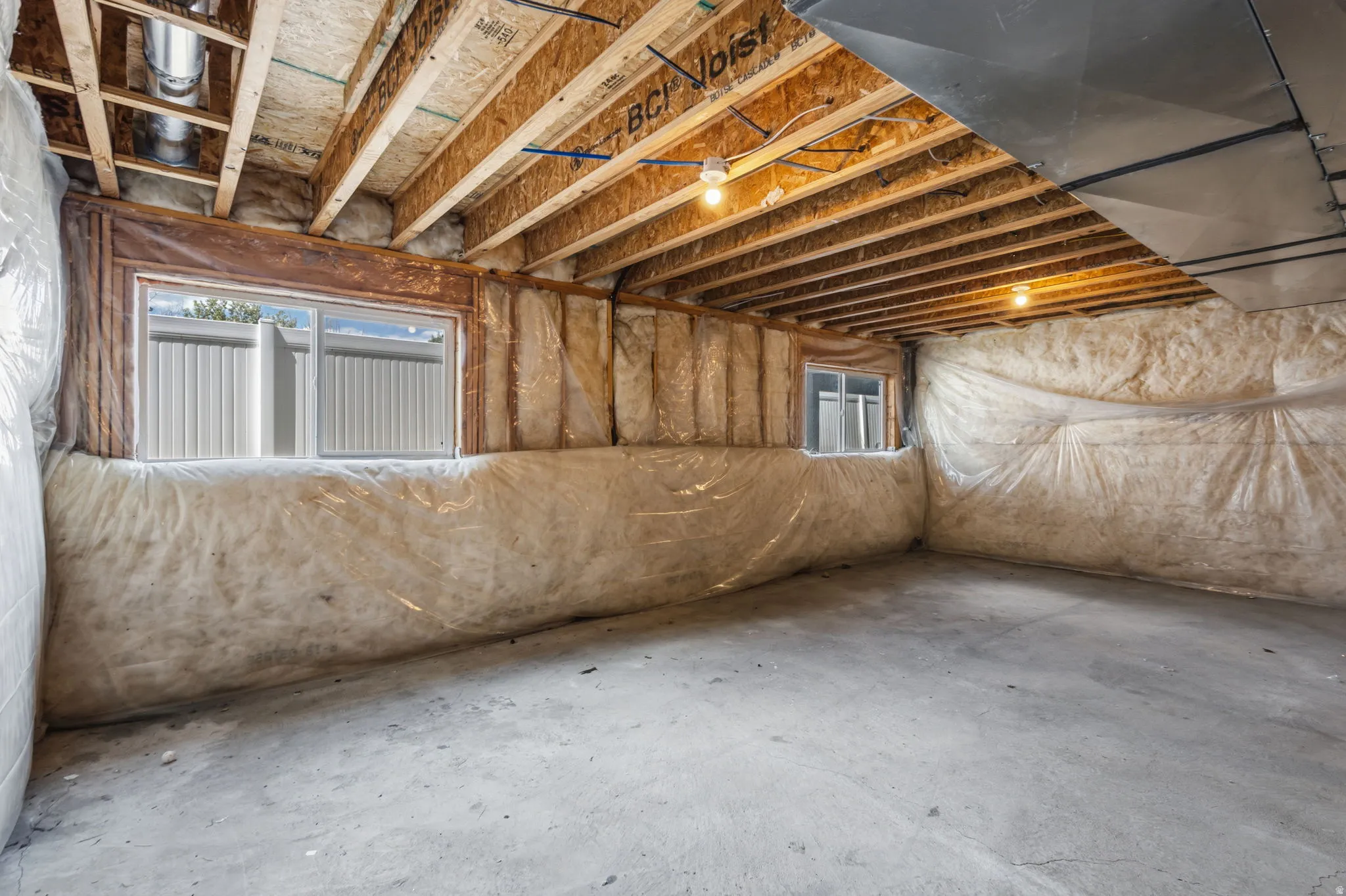 Unfinished lower level with exposed ceiling joists, two windows, concrete flooring, and insulated walls