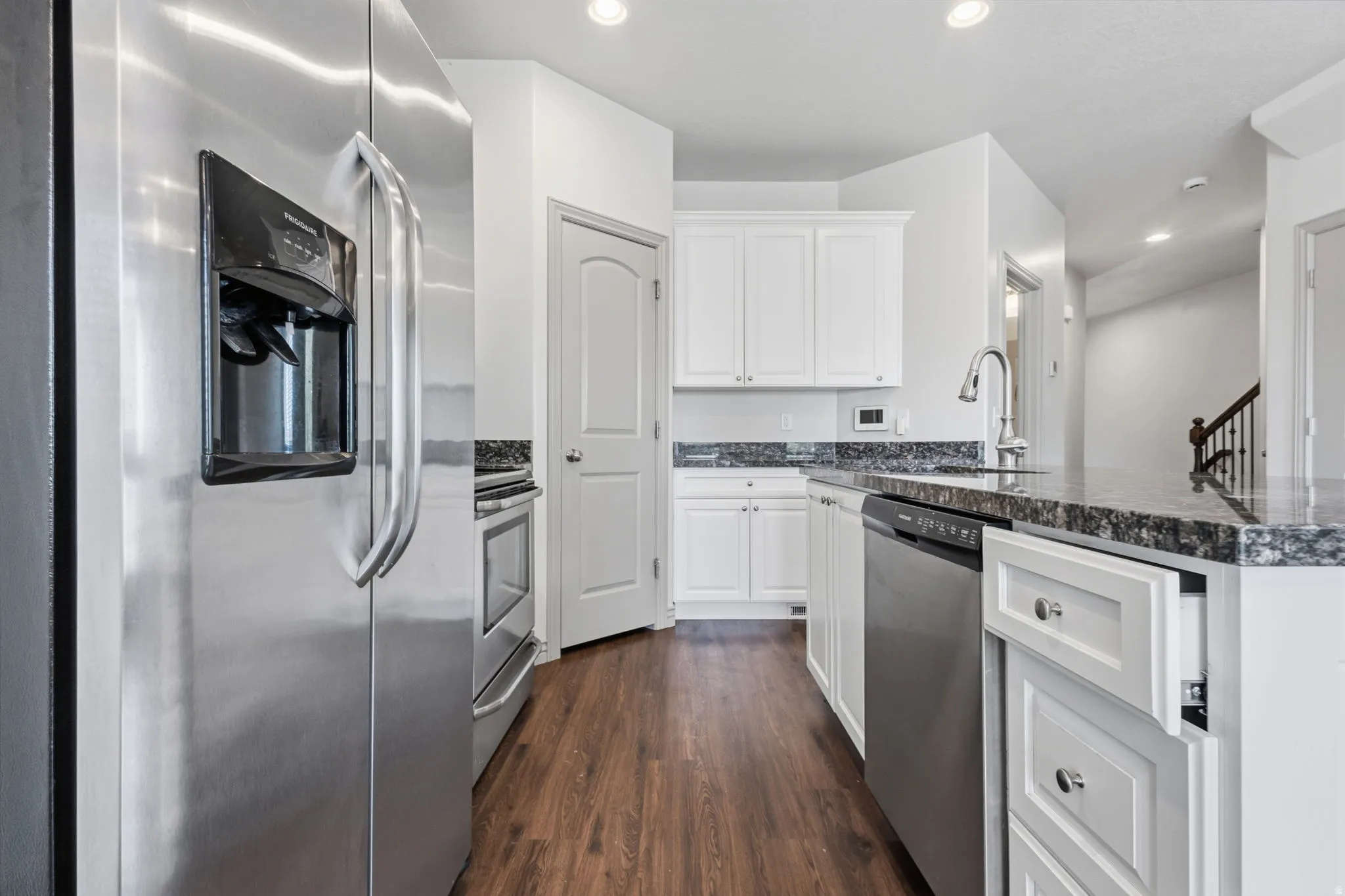 Kitchen featuring white cabinetry, dark stone countertops, stainless steel appliances, wood-finish flooring, and recessed lighting