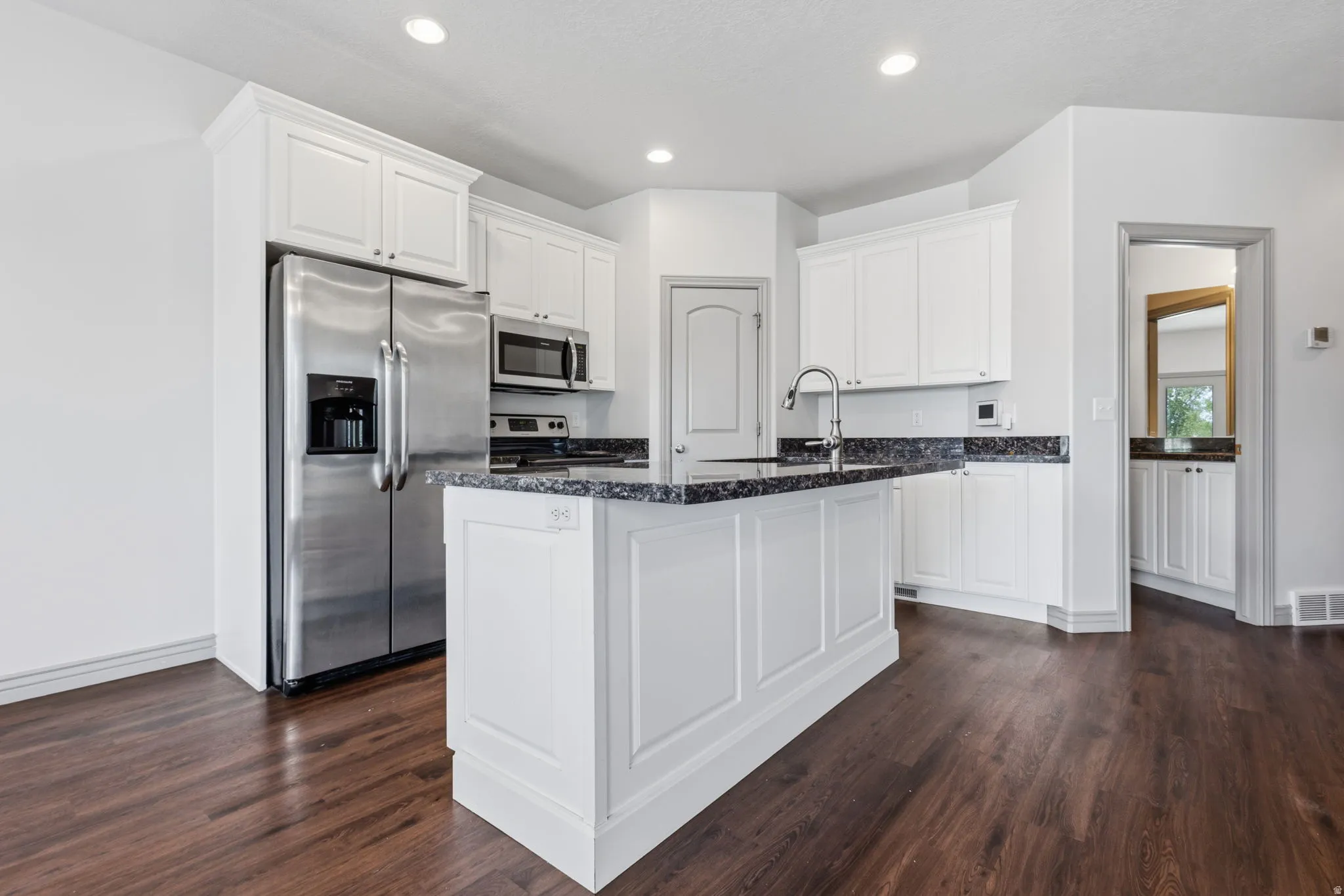 Kitchen featuring white cabinetry, dark stone-finish countertops, stainless steel appliances, a center island with sink, and wood-finish flooring