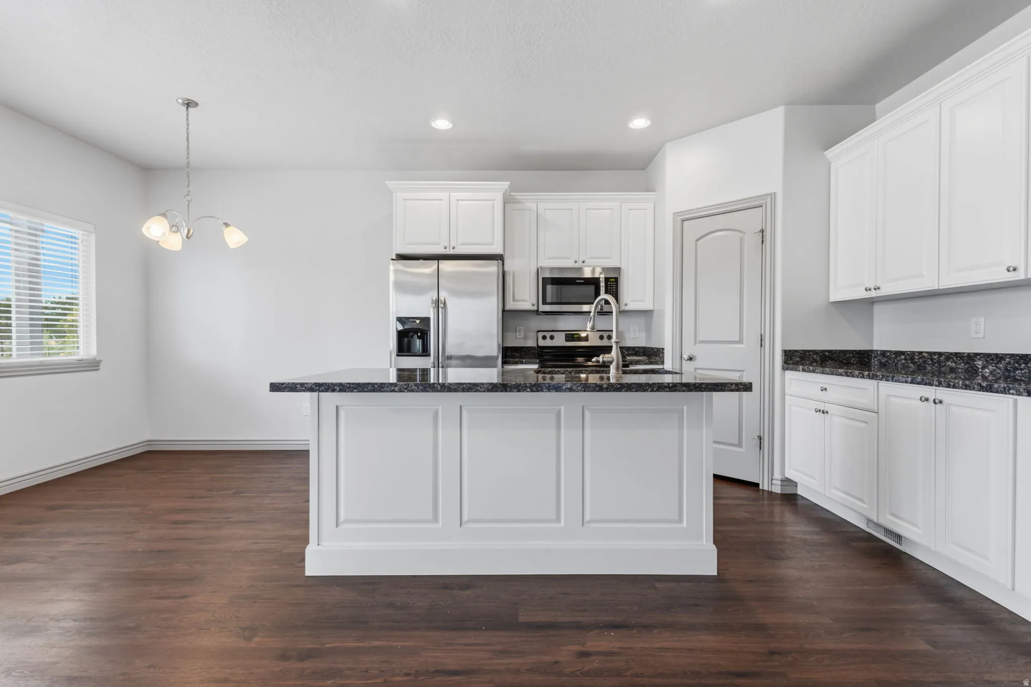 Kitchen featuring white cabinetry, dark speckled countertops, stainless steel appliances, and wood-finish flooring