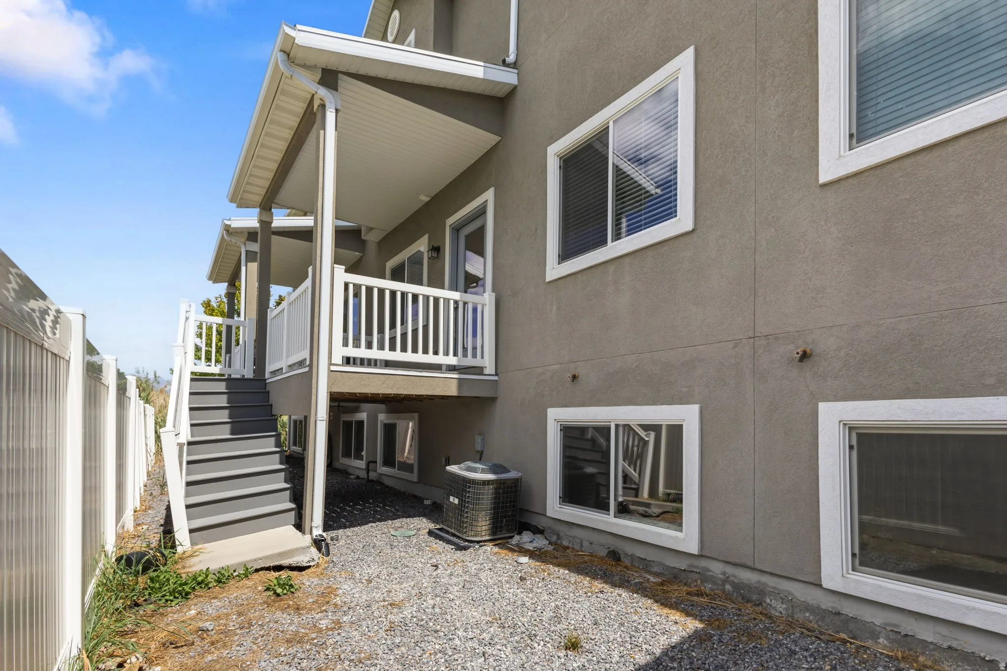 Stucco exterior with multiple windows, leading to an elevated balcony with white railings, and an exterior staircase