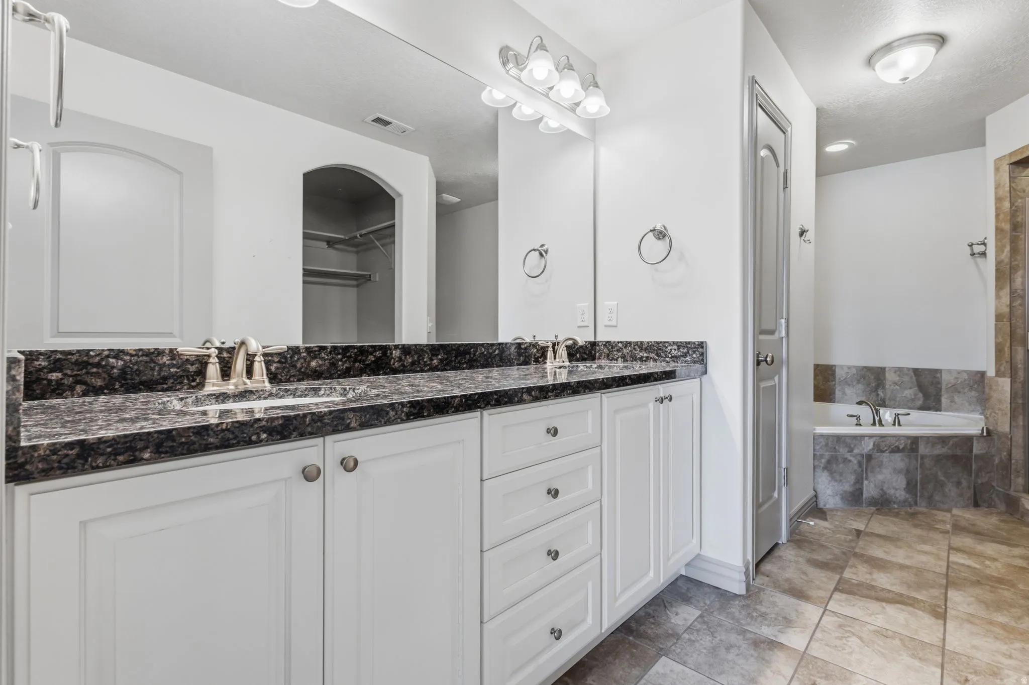 Dual vanity with dark stone countertop, white cabinetry, and brushed nickel fixtures