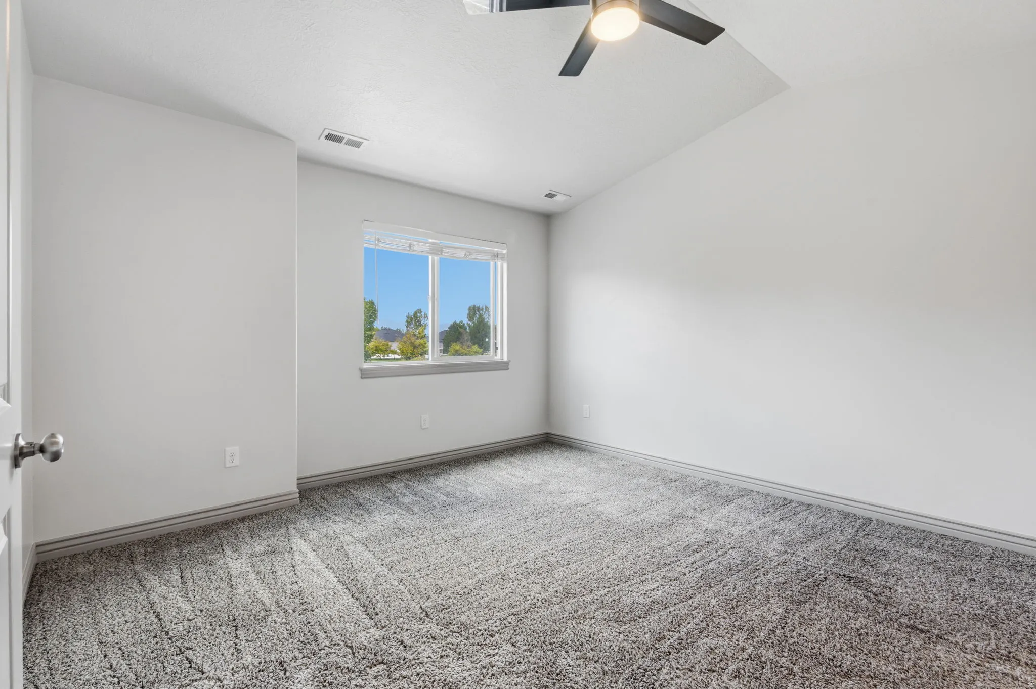 Vaulted ceiling with a ceiling fan, plush carpet flooring, and a large window with white trim