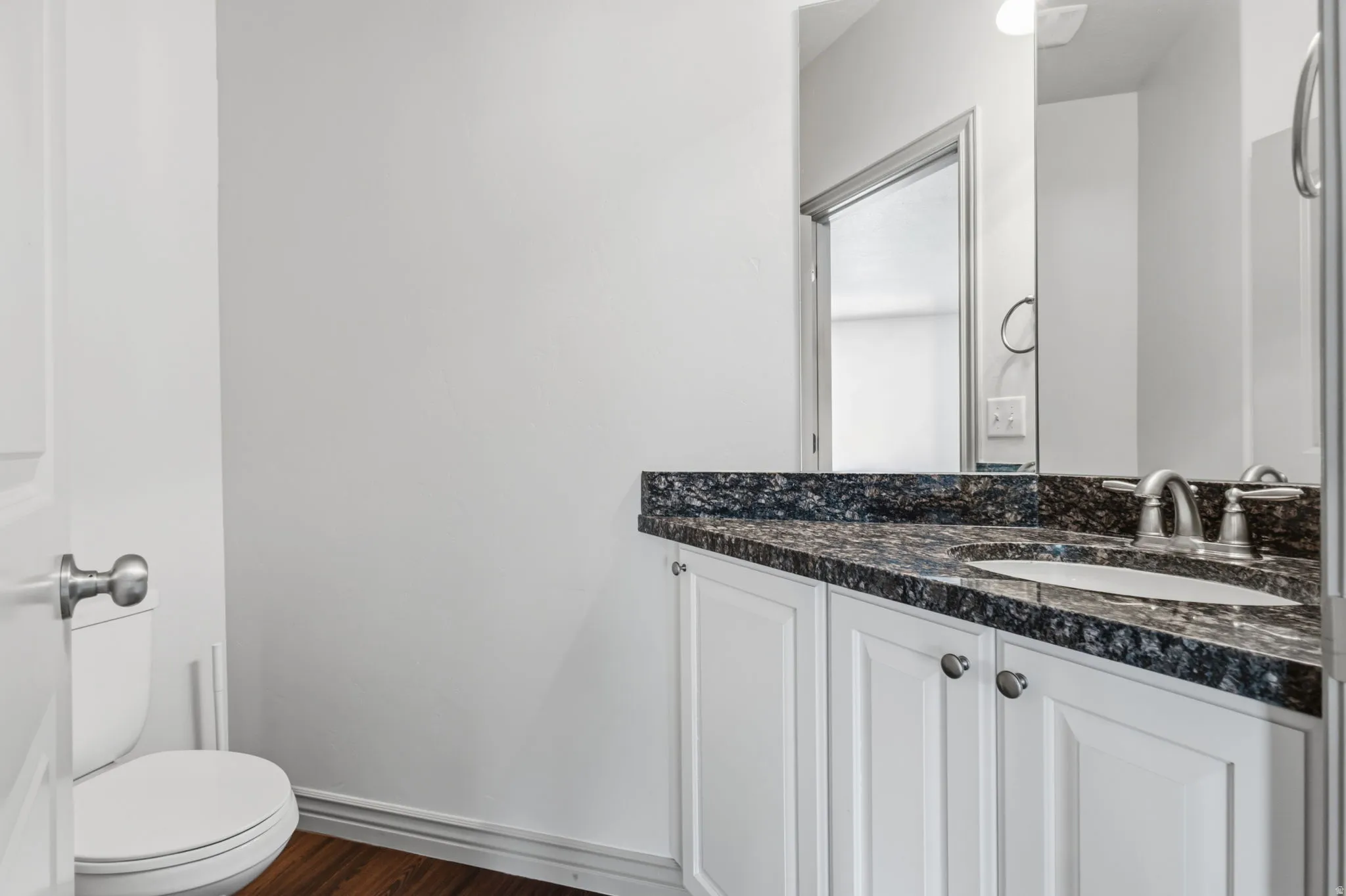 White vanity with dark stone countertop, undermount sink, and brushed nickel faucet