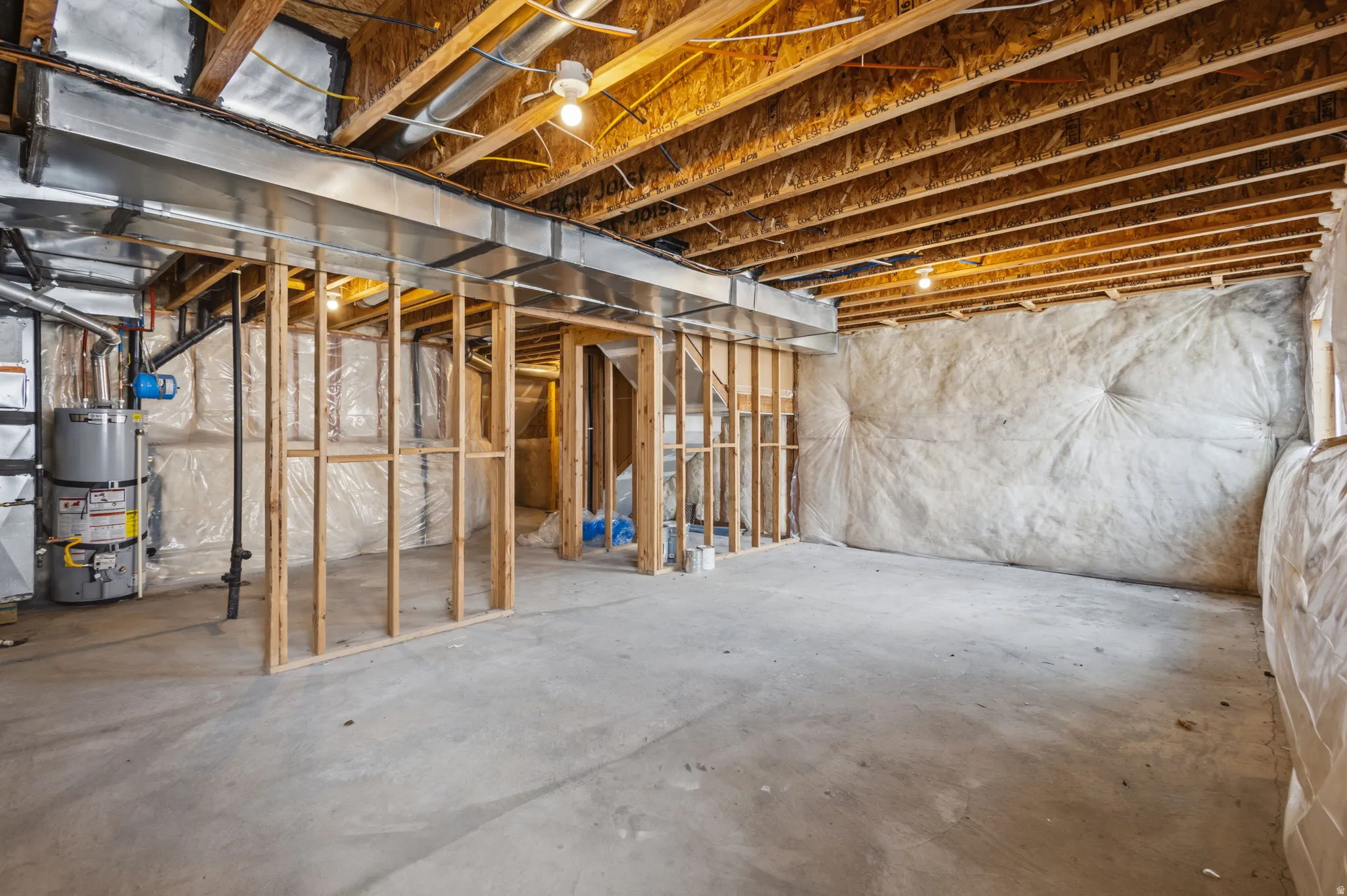 Unfinished basement with concrete flooring, exposed wood joists, and framed interior walls