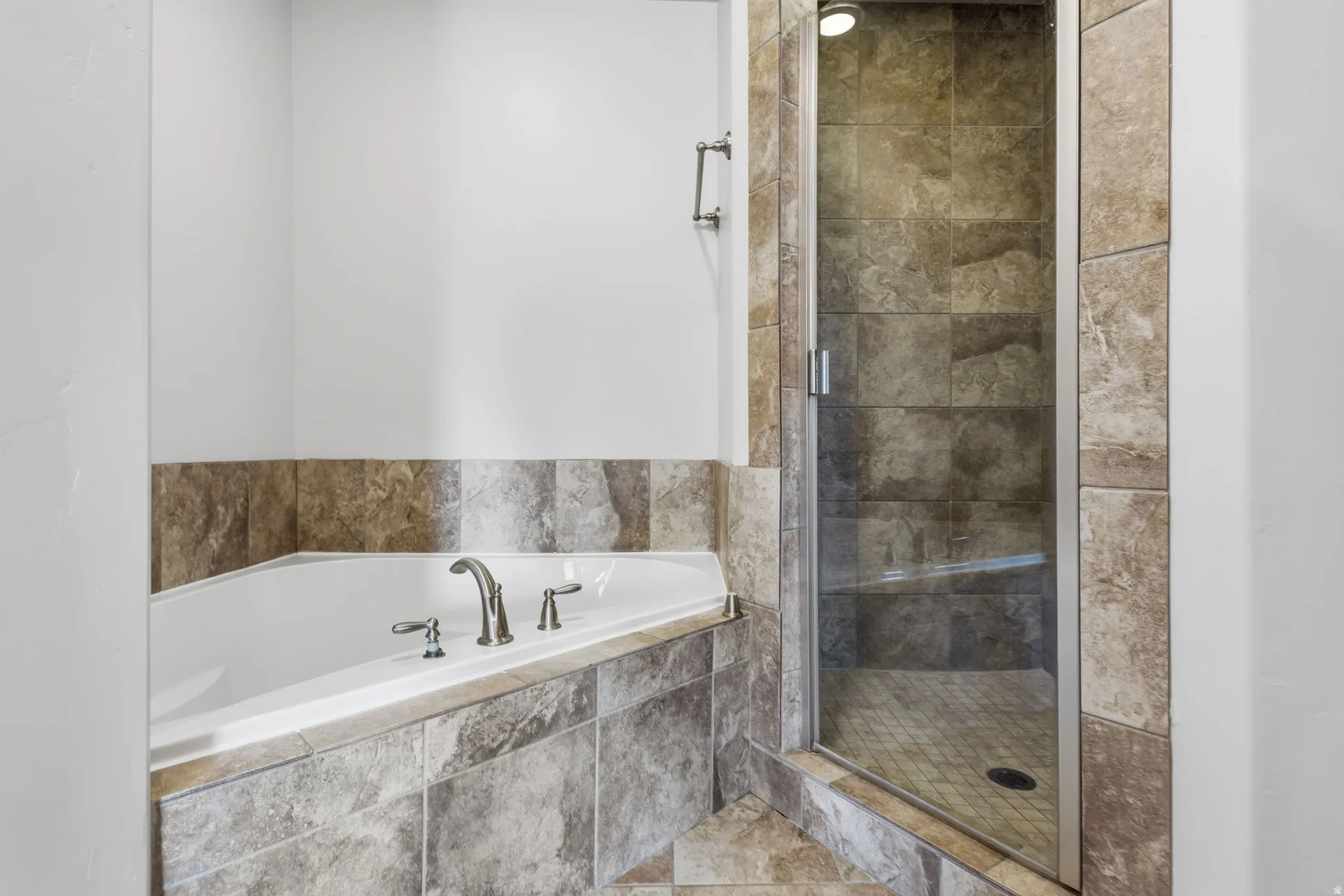 Soaking tub with deck-mounted fixtures, separate tiled shower with glass enclosure, and tiled walls with a light-toned finish
