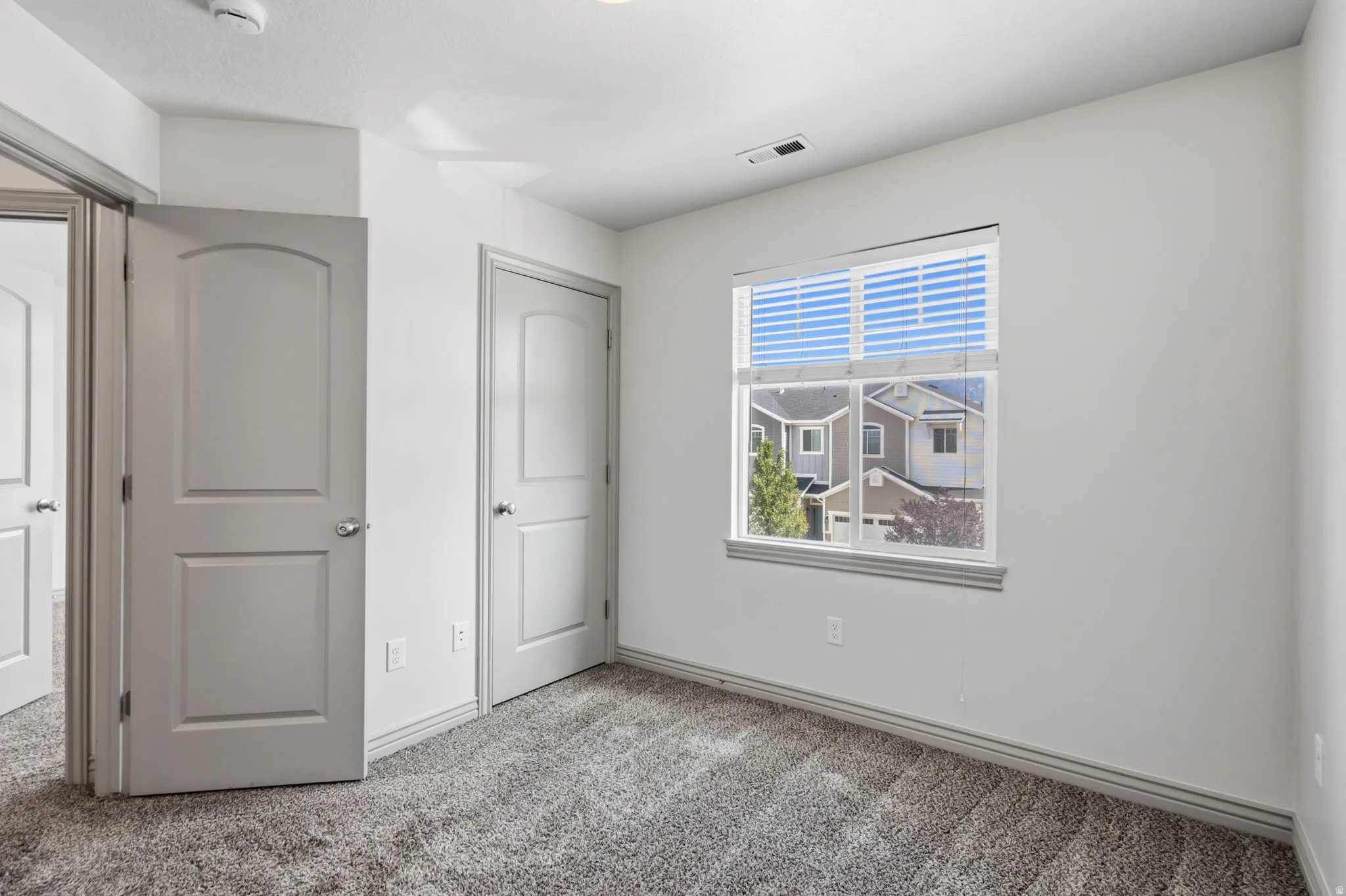 Recessed lighting, gray carpeting, a single window with blinds, and multiple interior doors with arch paneling