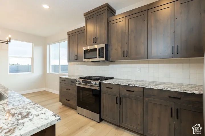 Kitchen featuring dark wood-finish cabinetry, light-toned countertops, stainless steel appliances, a white tile backsplash, and light wood-finish flooring