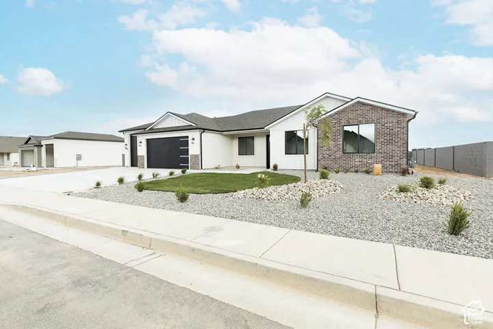 Contemporary exterior featuring white siding, brick accents, a black garage door, and a low-maintenance landscape design
