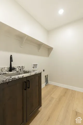 Laundry area featuring wood-finish flooring, a dark wood-finish vanity with a stainless steel sink, and light-toned countertop