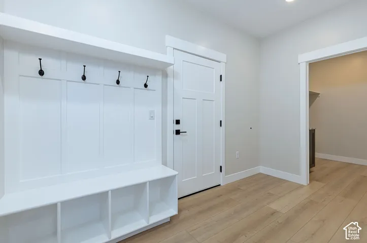 Mudroom featuring built-in cubbies with individual storage compartments, shaker-style cabinetry with white finish, four wall-mounted hooks for coats and accessories, and wood-finish flooring throughout the space