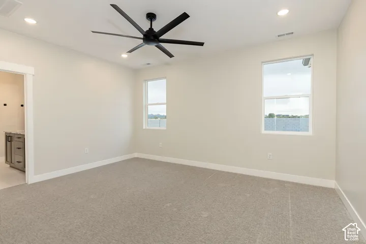 Spacious room featuring neutral carpeting, recessed lighting, a modern ceiling fan, and two large windows