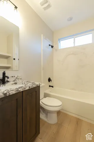 Wood-finish flooring, dark wood-tone vanity with stone-patterned countertop, matte black fixtures, bathtub with patterned surround, and an upper window