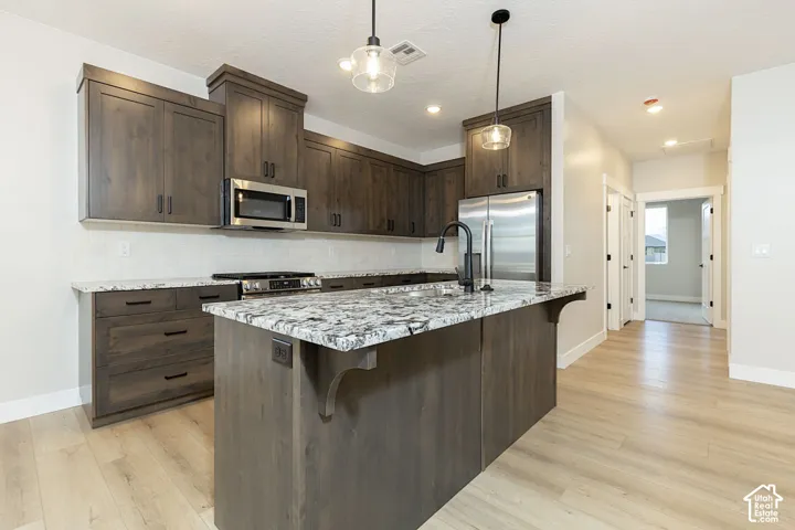 Kitchen featuring dark wood-finish cabinetry, granite countertops, a tile backsplash, stainless steel appliances, and a central island with pendant lighting