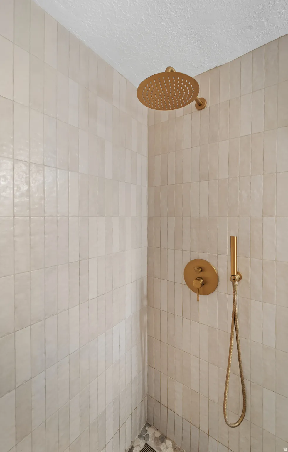 Shower featuring light-toned vertical subway tile, a rain showerhead, a hand-held shower, and pebble-tiled flooring