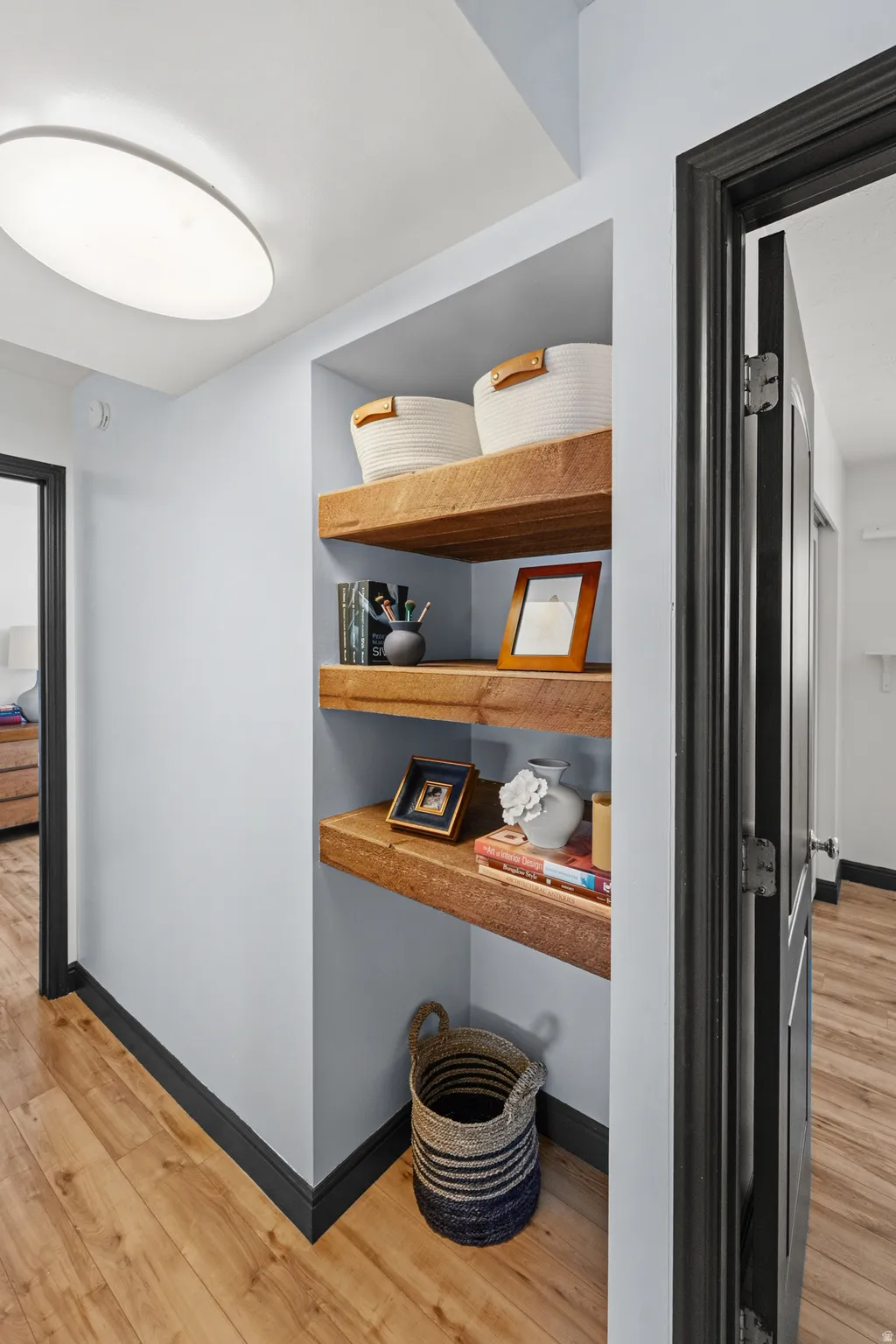 Recessed shelving with wood-finish shelves, light wood-finish flooring, dark trim, and a flush-mount ceiling light
