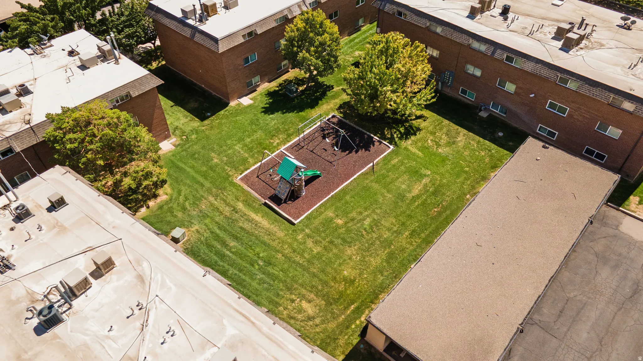 Expansive green space featuring a playground with a slide and climbing structure, surrounded by mature trees