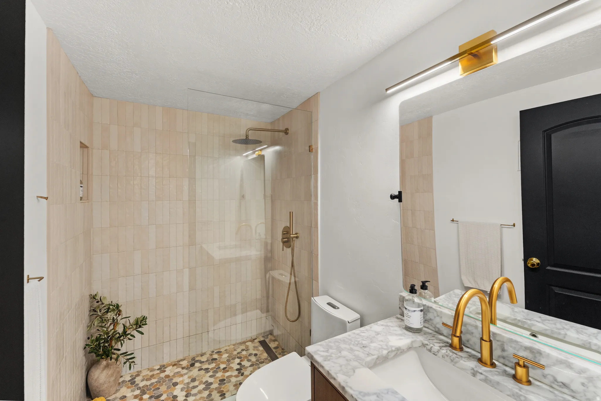 Glass-enclosed shower with vertical tile surround and pebble-finish flooring