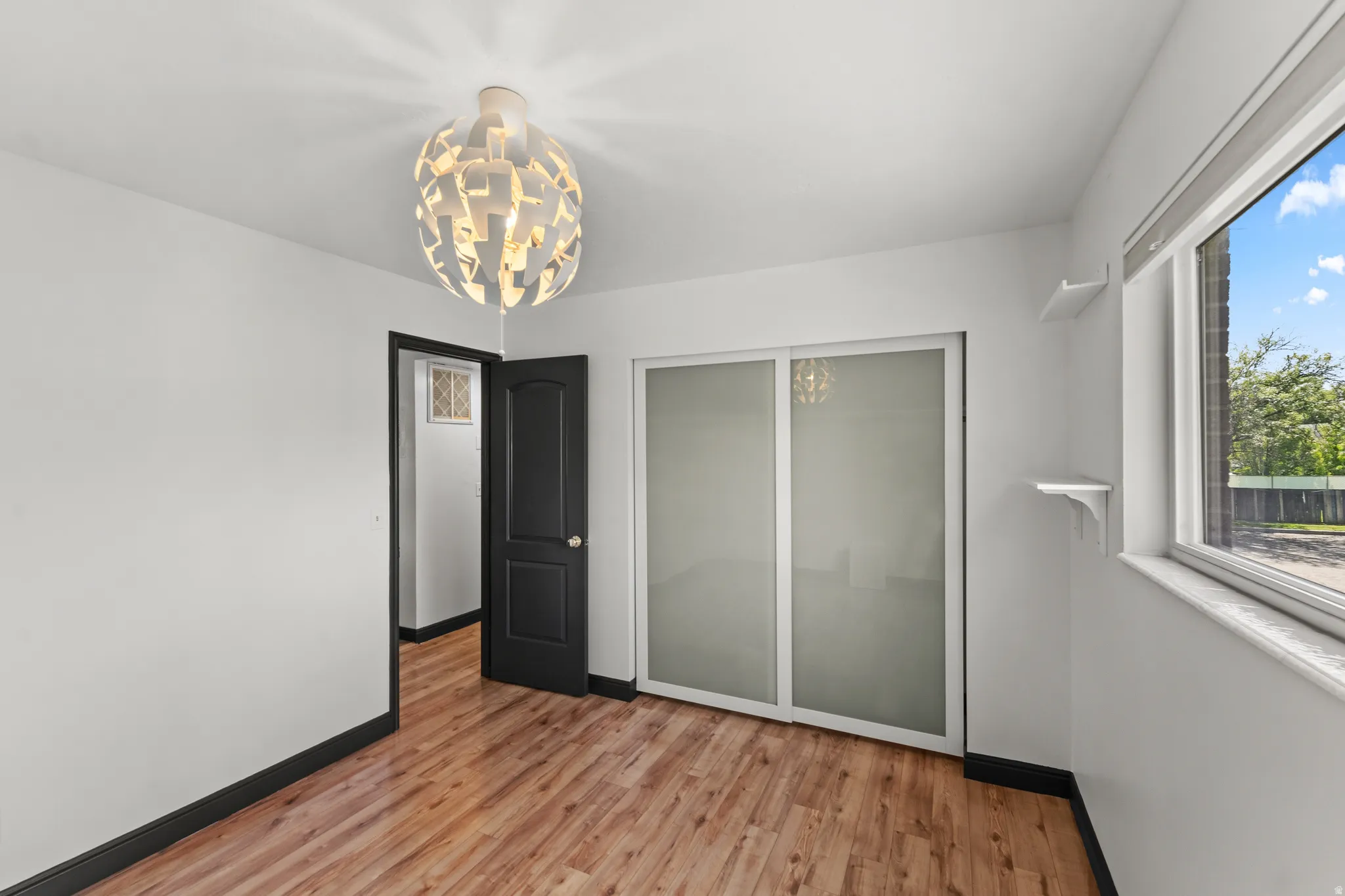 Wood-finish flooring, white walls, black trim, frosted glass sliding closet doors, and an overhead light fixture