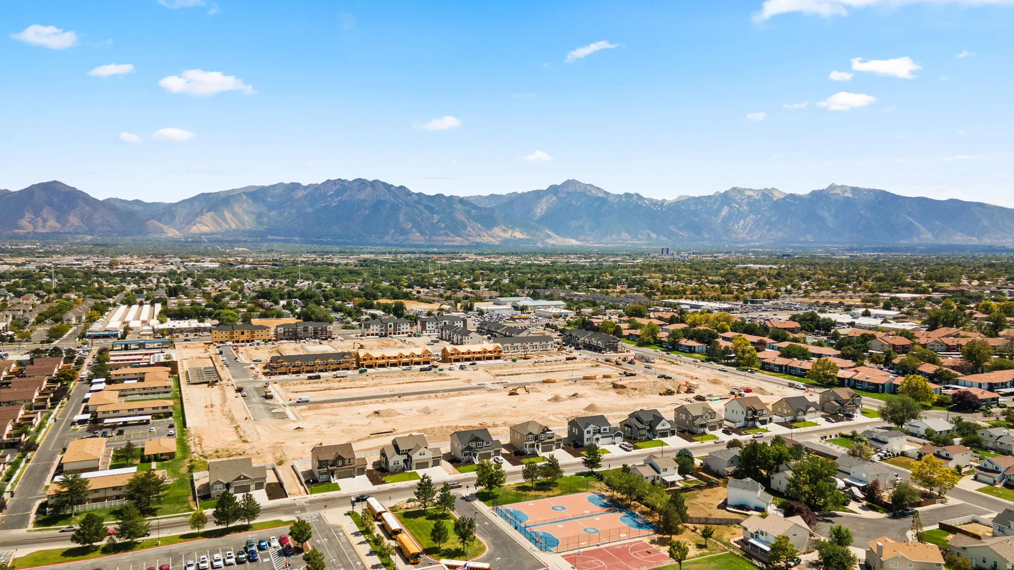 Expansive development site with mountain backdrop, surrounded by established residential areas and commercial structures